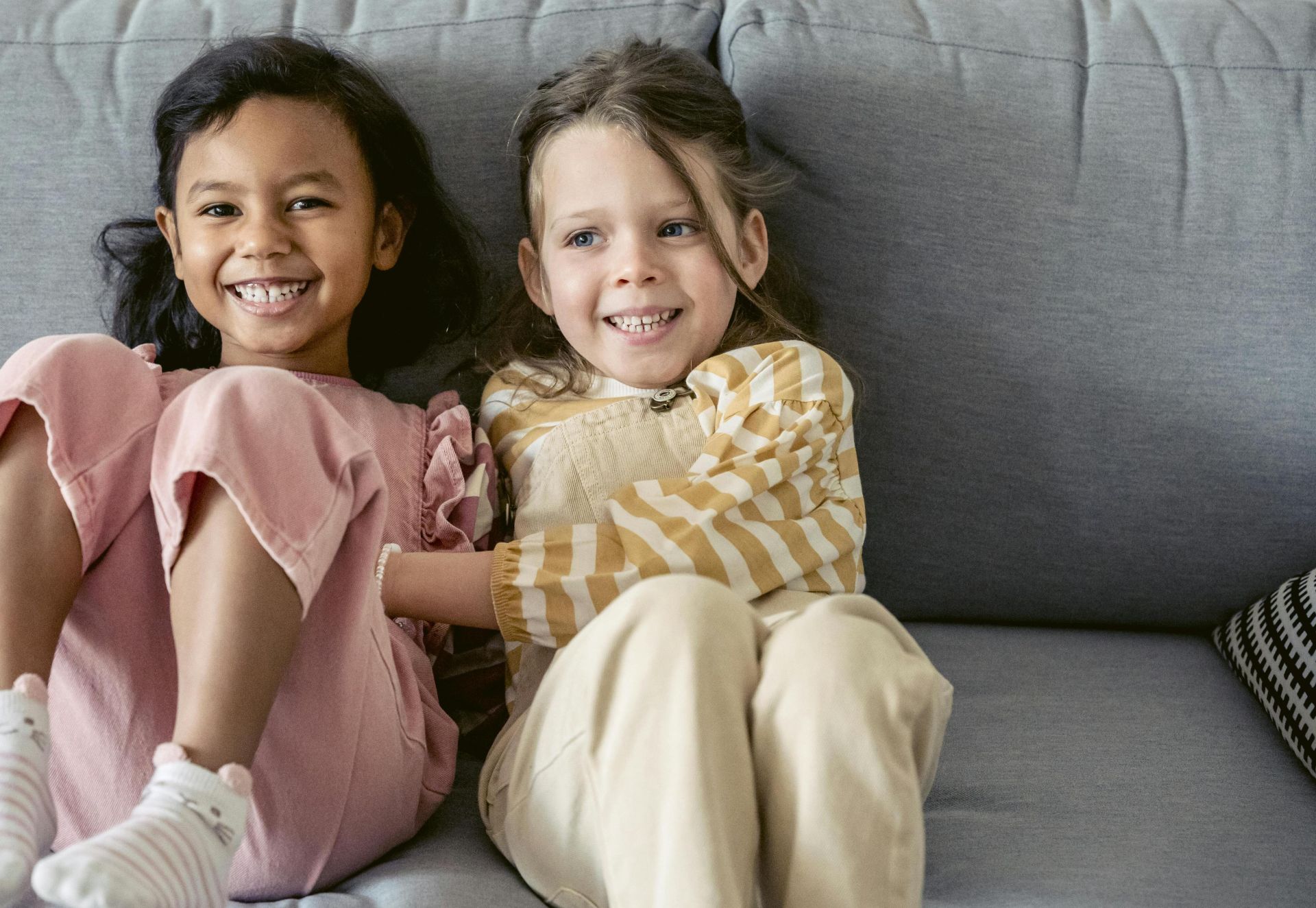 Cheerful best multiracial friends in striped clothes interacting on couch in living room in house
