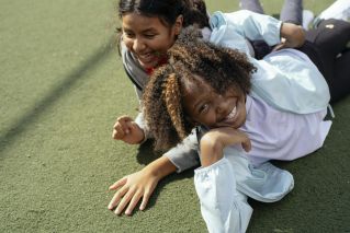 Cheerful multiracial girls lying on sports ground and smiling while spending sunny day together