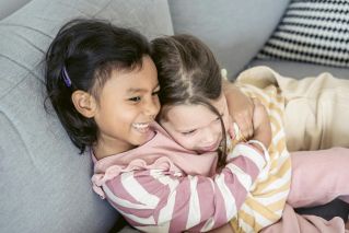 Two young girls embracing with smiles, showing friendship and joy indoors.